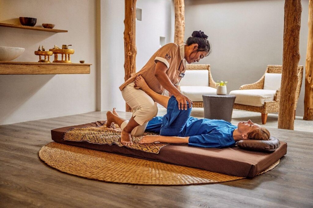 Praticienne réalisant un massage thaï traditionnel sur un matelas au sol